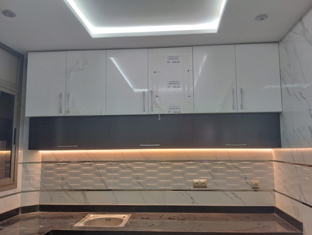 Cuisine avec meubles blancs laqués, faux plafond lumineux LED et crédence en marbre — réalisée par Jouissance